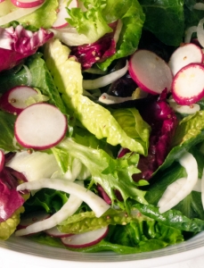 close up on bowl of salad with mixed greens and radish slices